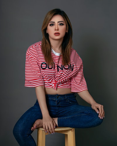 Dressed in red and white striped shirt and blue denim jeans women sat on the grey chair
